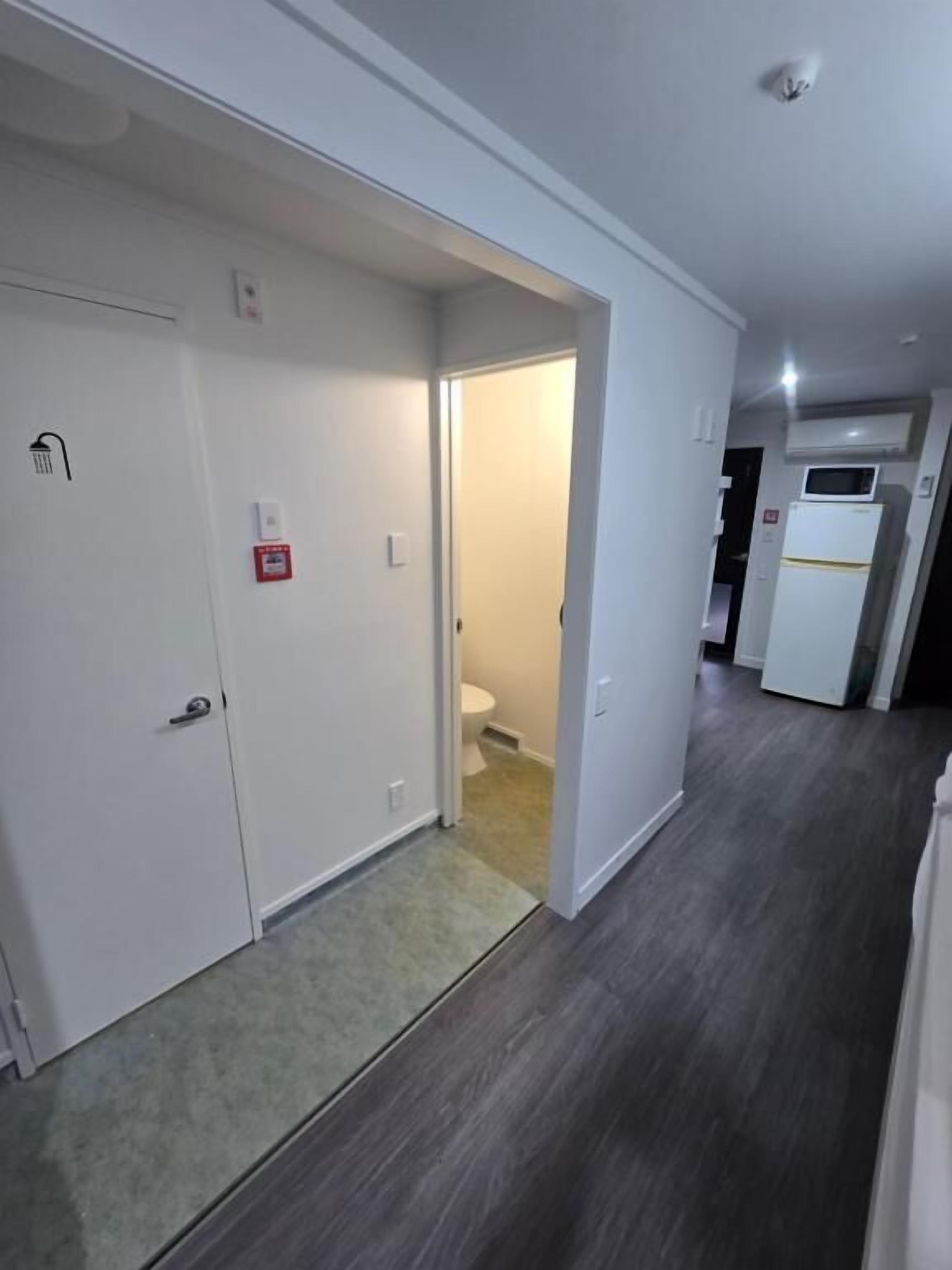 A hallway with a door leading to a bathroom, a microwave, and a refrigerator in the kitchen area.