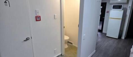 A hallway with a door leading to a bathroom, a microwave, and a refrigerator in the kitchen area.