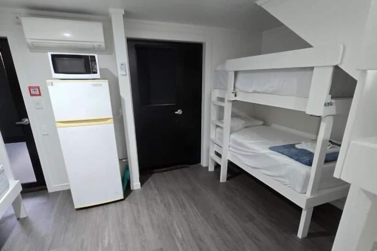 A compact room with a bunk bed, a white refrigerator, and a microwave.