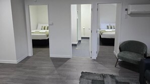 A modern hotel room with a grey carpet, two beds with white linens, a green armchair, and a visible air conditioning unit. - Microtel Lodge (Hamilton)