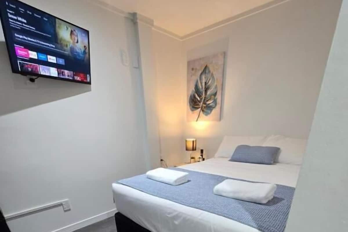 A modern hotel room with a large bed, a flat-screen TV mounted on the wall, and a painting on the wall.