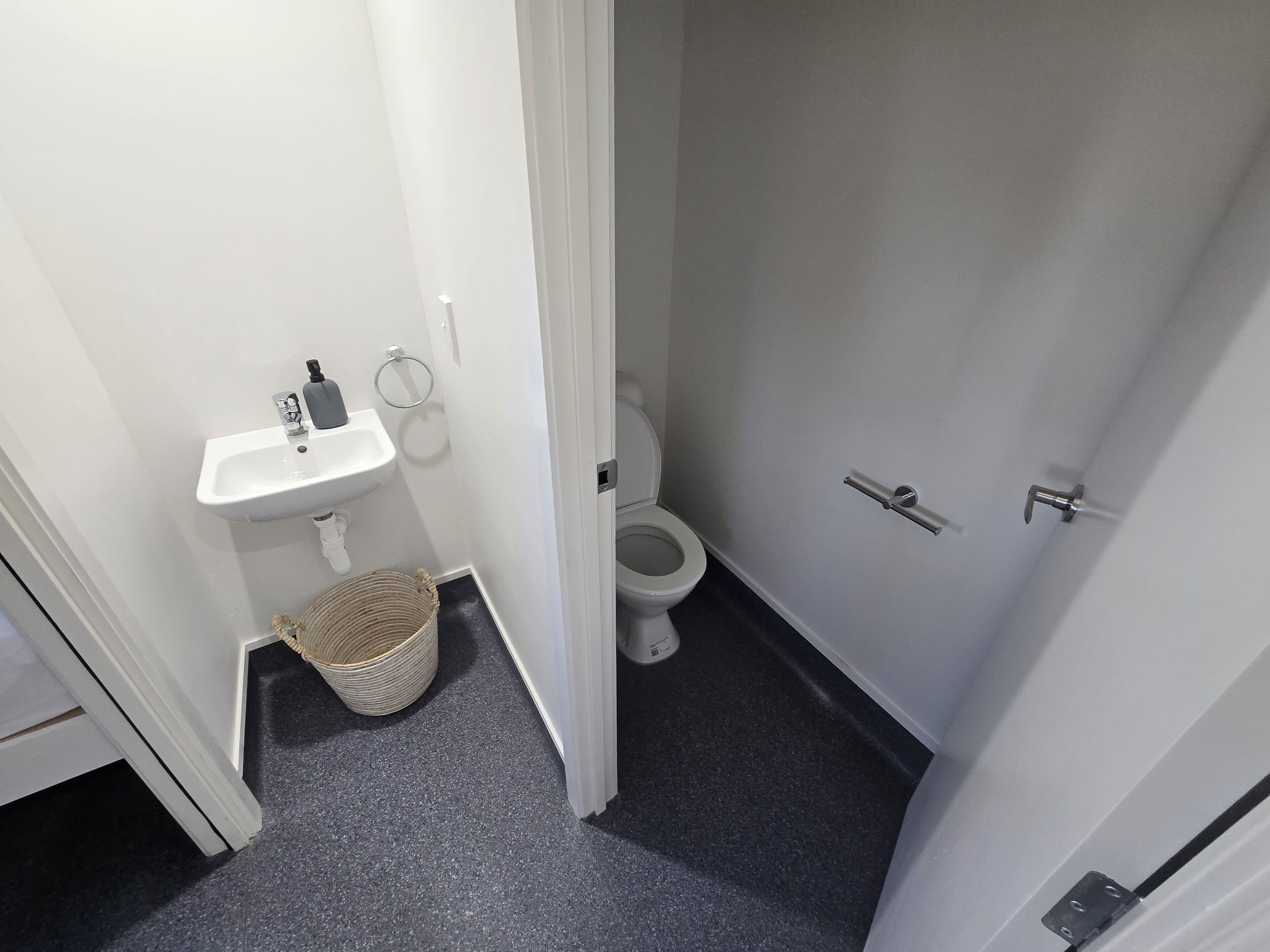 Une petite salle de bain avec un lavabo blanc, des toilettes et un panier posé sur le sol.