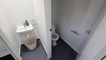 Une petite salle de bain avec un lavabo blanc, des toilettes et un panier posé sur le sol.