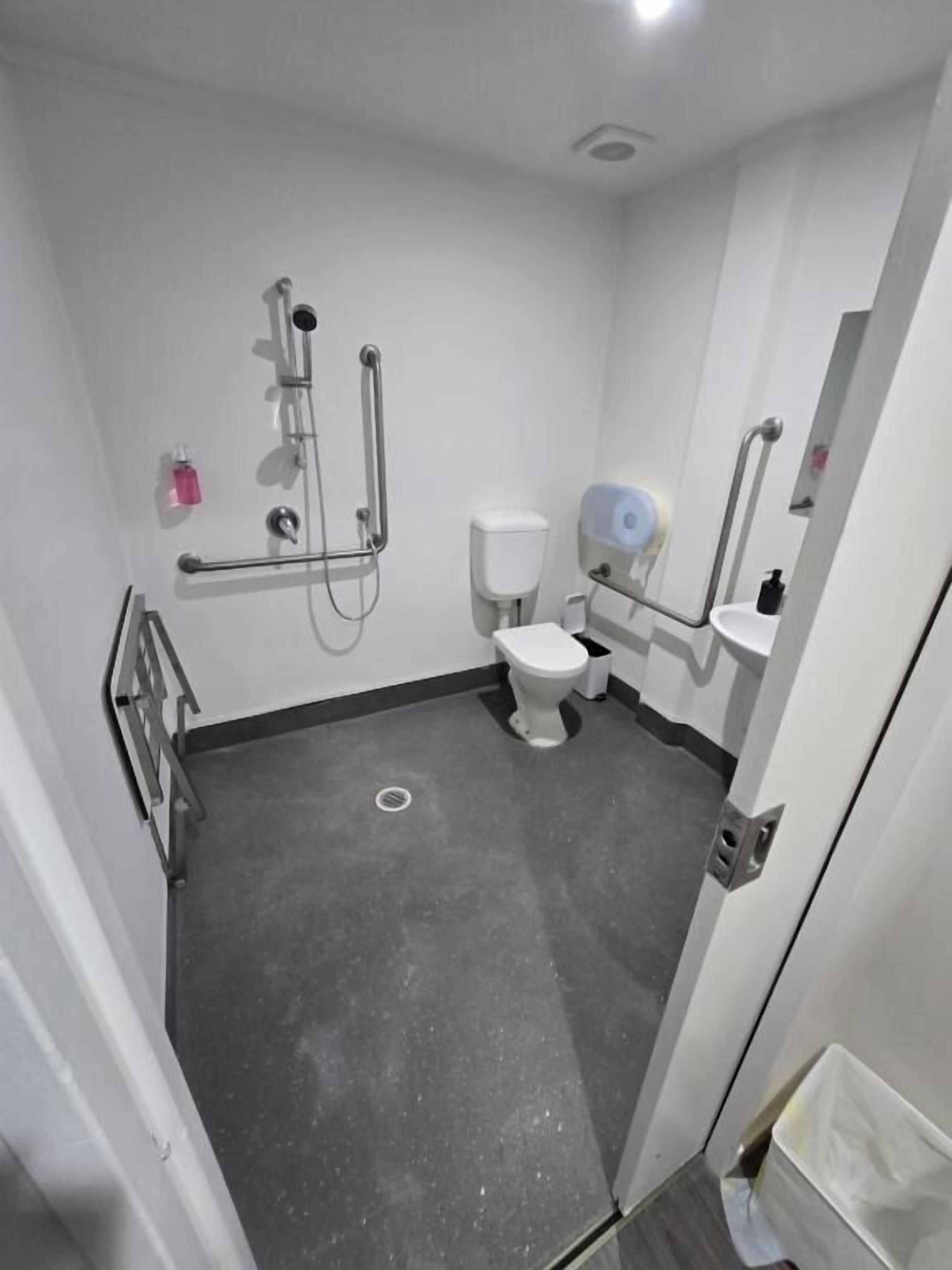 A small, modern bathroom with a white toilet, a shower with grab bars, and a hand dryer.