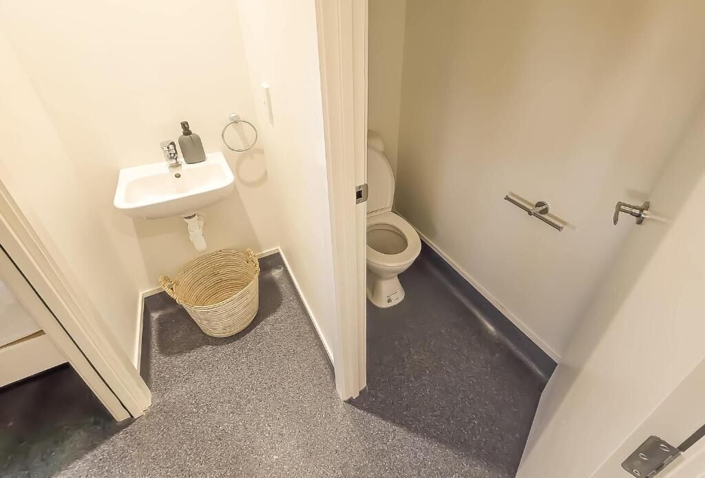 Un baño pequeño con un lavamanos blanco, un inodoro y una cesta en el suelo.