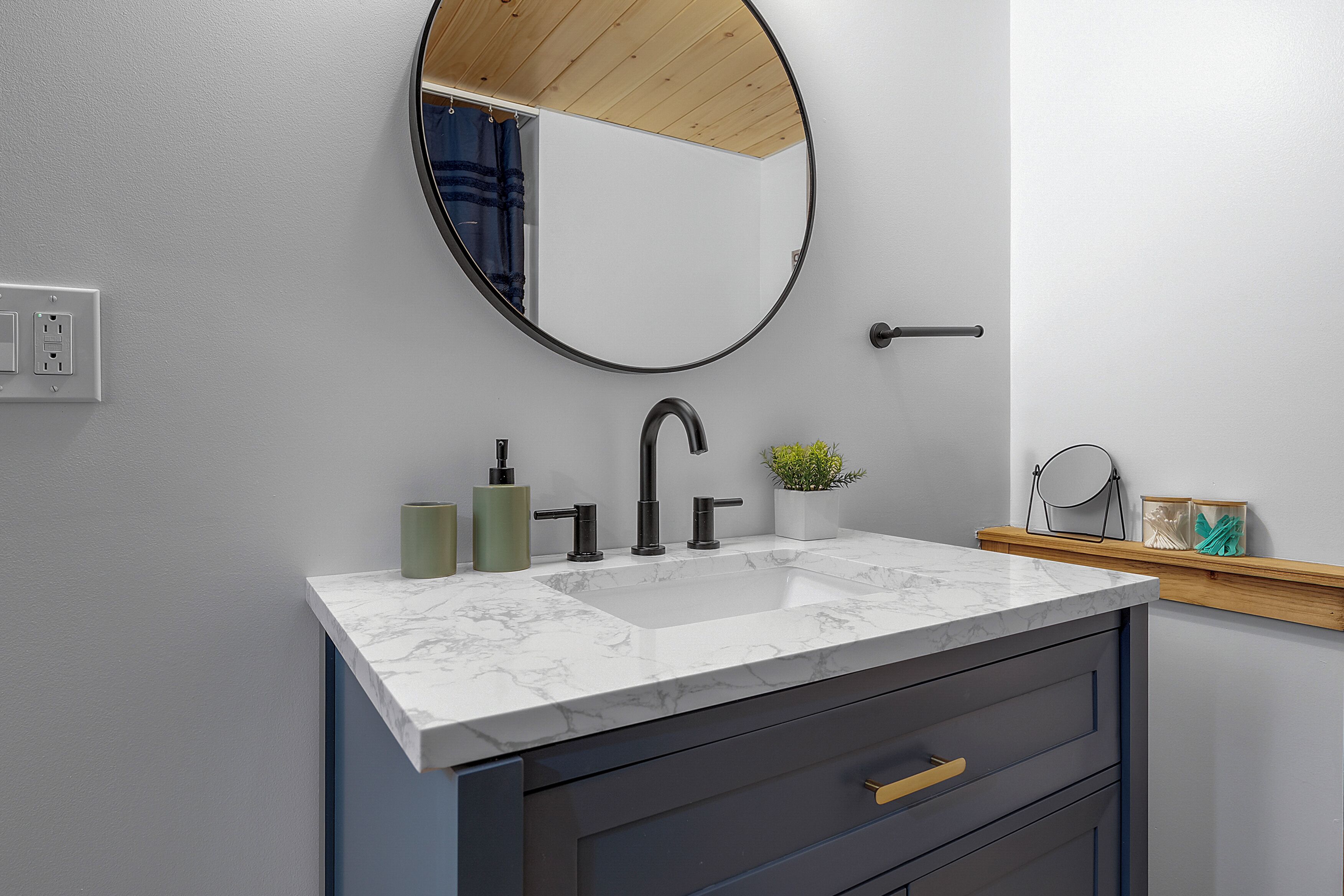 A bathroom with a white marble sink, a round mirror, and a wooden shelf with toiletries.