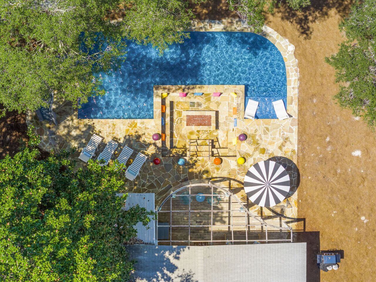 Vue aérienne d’un espace piscine avec une terrasse en pierre, des chaises longues et un moulin à vent.