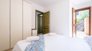 A bedroom with a bed, a wardrobe, a bathroom, and a door leading to an outdoor area. - Alessandra’s Garden Hideaway (Simius)