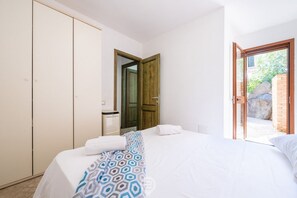 A bedroom with a bed, a wardrobe, a bathroom, and a door leading to an outdoor area. - Alessandra’s Garden Hideaway (Simius)