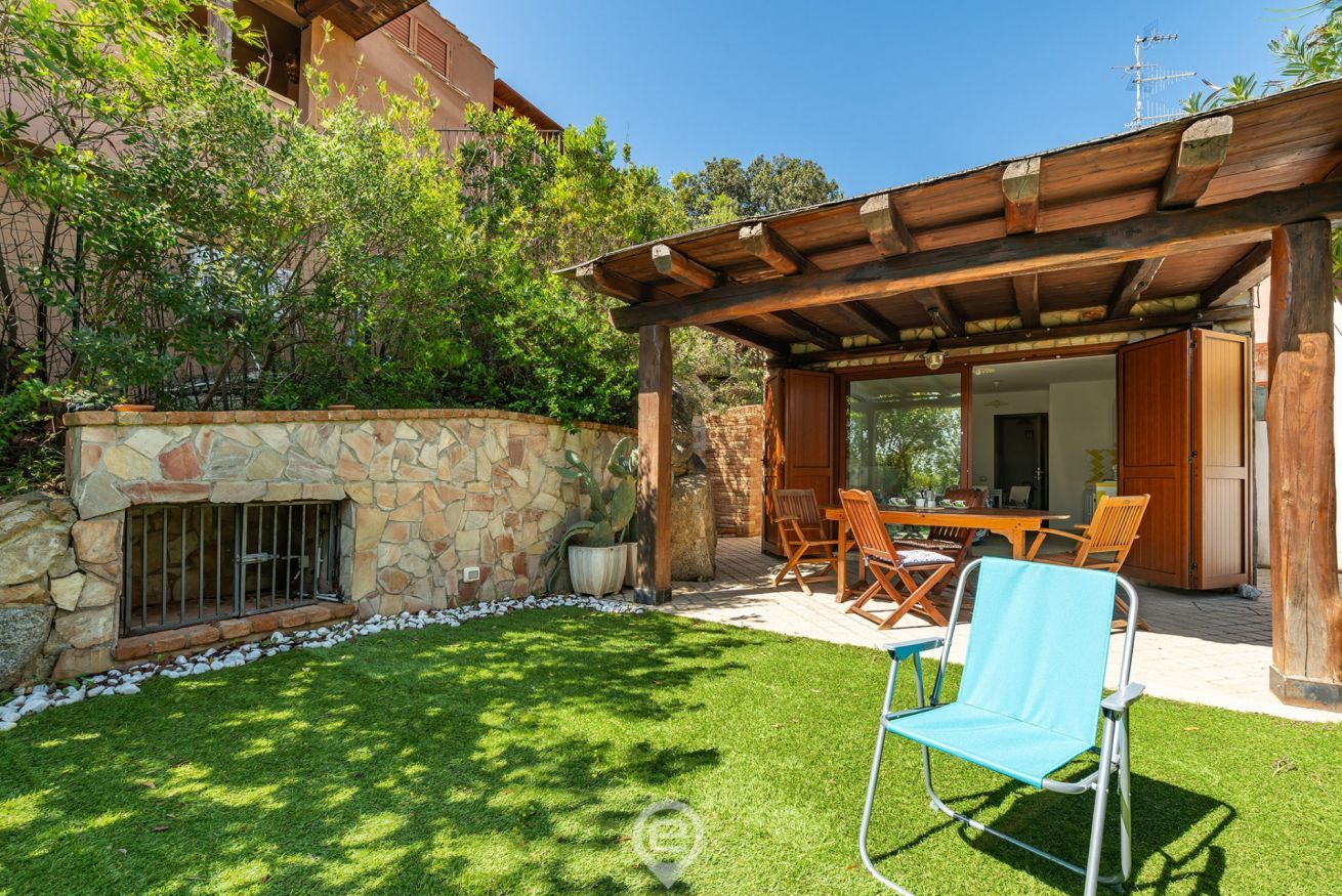 Une terrasse avec un mur en pierre, une pergola en bois et un espace détente comprenant des chaises et une table.
