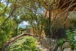 Un jardin avec un mur de pierre, une pergola et une vue sur la mer.