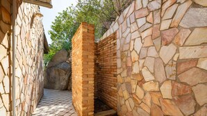 A stone-walled outdoor area with a brick structure, possibly a sauna or hot tub, surrounded by a paved floor. - Alessandra’s Garden Hideaway (Simius)