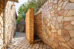A stone-walled outdoor area with a brick structure, possibly a sauna or hot tub, surrounded by a paved floor. - Alessandra’s Garden Hideaway (Simius)