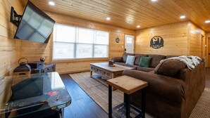 A cozy cabin interior with a wooden interior, a sofa, a coffee table, a TV mounted on the wall, and a fireplace. - Pigeon Forge Comfort - 3 Bed with Fenced in yard (Pigeon Forge)
