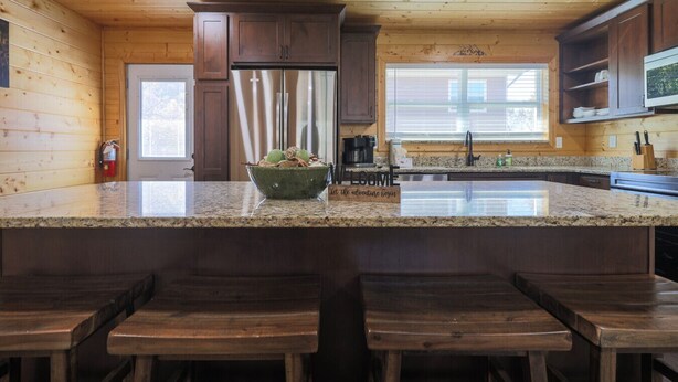 A kitchen with a granite countertop, wooden cabinets, a stainless steel refrigerator, and a 'Welcome' sign. - Pigeon Forge Comfort - 3 Bed with Fenced in yard (Pigeon Forge)