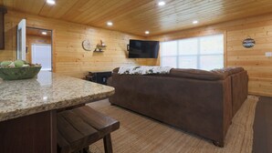 A cozy cabin interior with a wooden ceiling, a stone countertop, a brown sofa, and a television mounted on the wall. - Pigeon Forge Comfort - 3 Bed with Fenced in yard (Pigeon Forge)