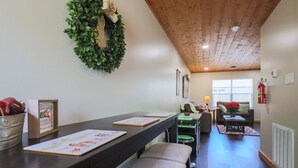 Un salón acogedor con techo de madera, chimenea, comedor con una mesa larga y una zona de estar confortable.