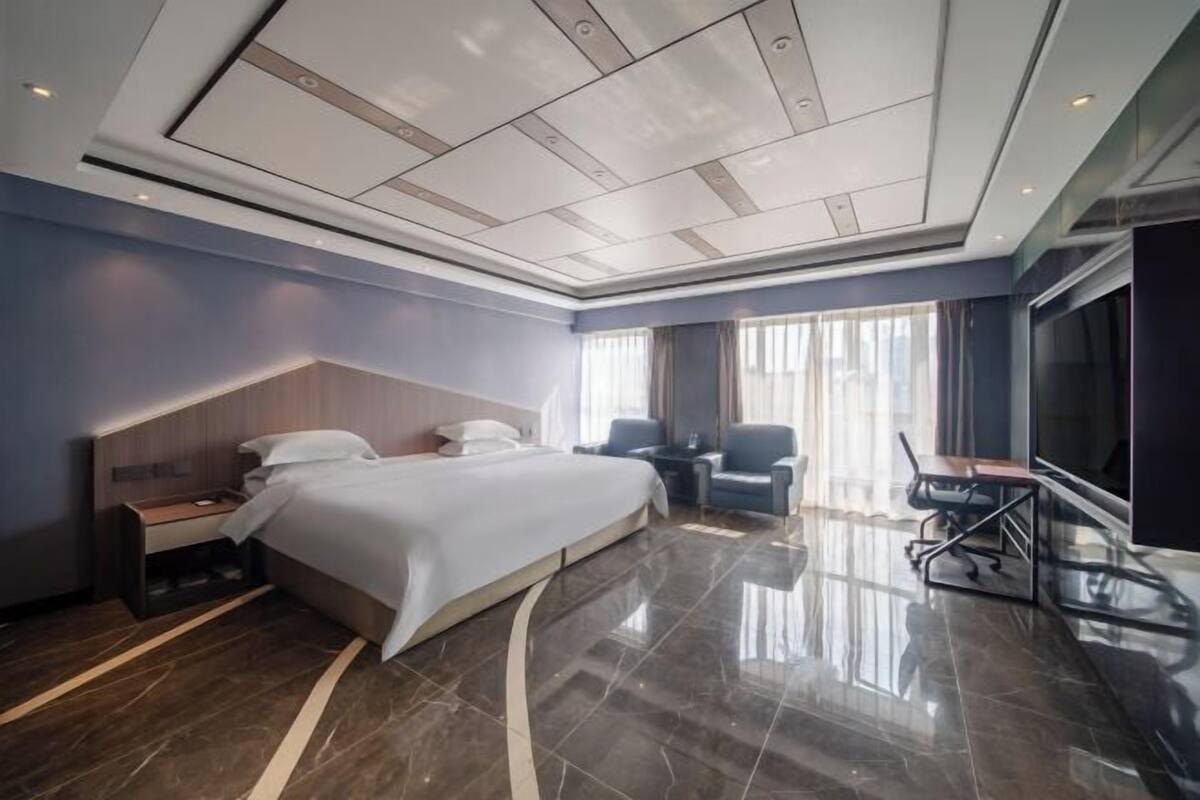 Ein modernes Hotelzimmer mit einem großen Bett, einem Schreibtisch, einem Stuhl, einem Fernseher und einem Fenster mit Vorhängen.