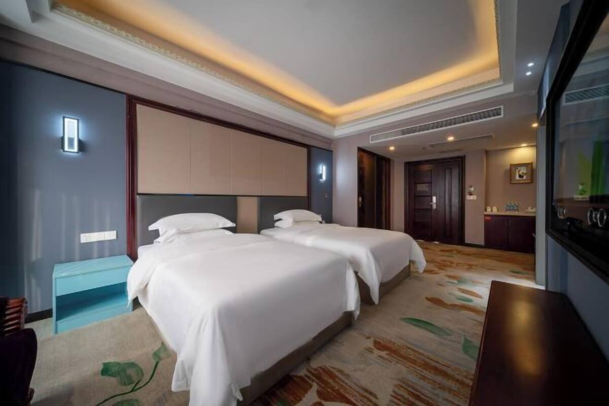 Ein Hotelzimmer mit zwei Betten, einem kleinen Schreibtisch, einem Badezimmer und einer Küchenzeile.