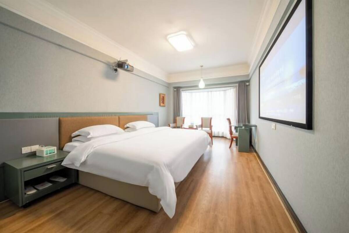 Ein Hotelzimmer mit Bett, Nachttisch, Lampe und einem großen Fenster.