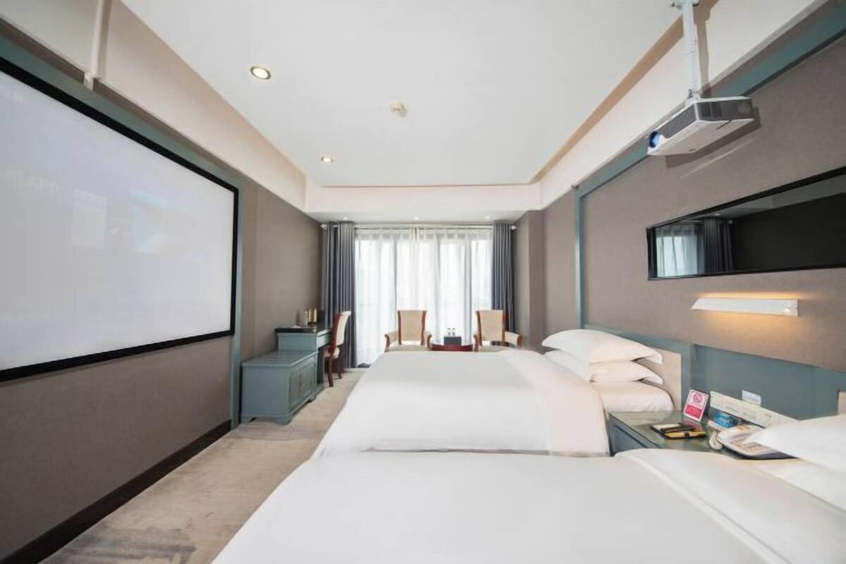 Ein Hotelzimmer mit Bett, Schreibtisch, Stuhl, Fernseher und Projektor.