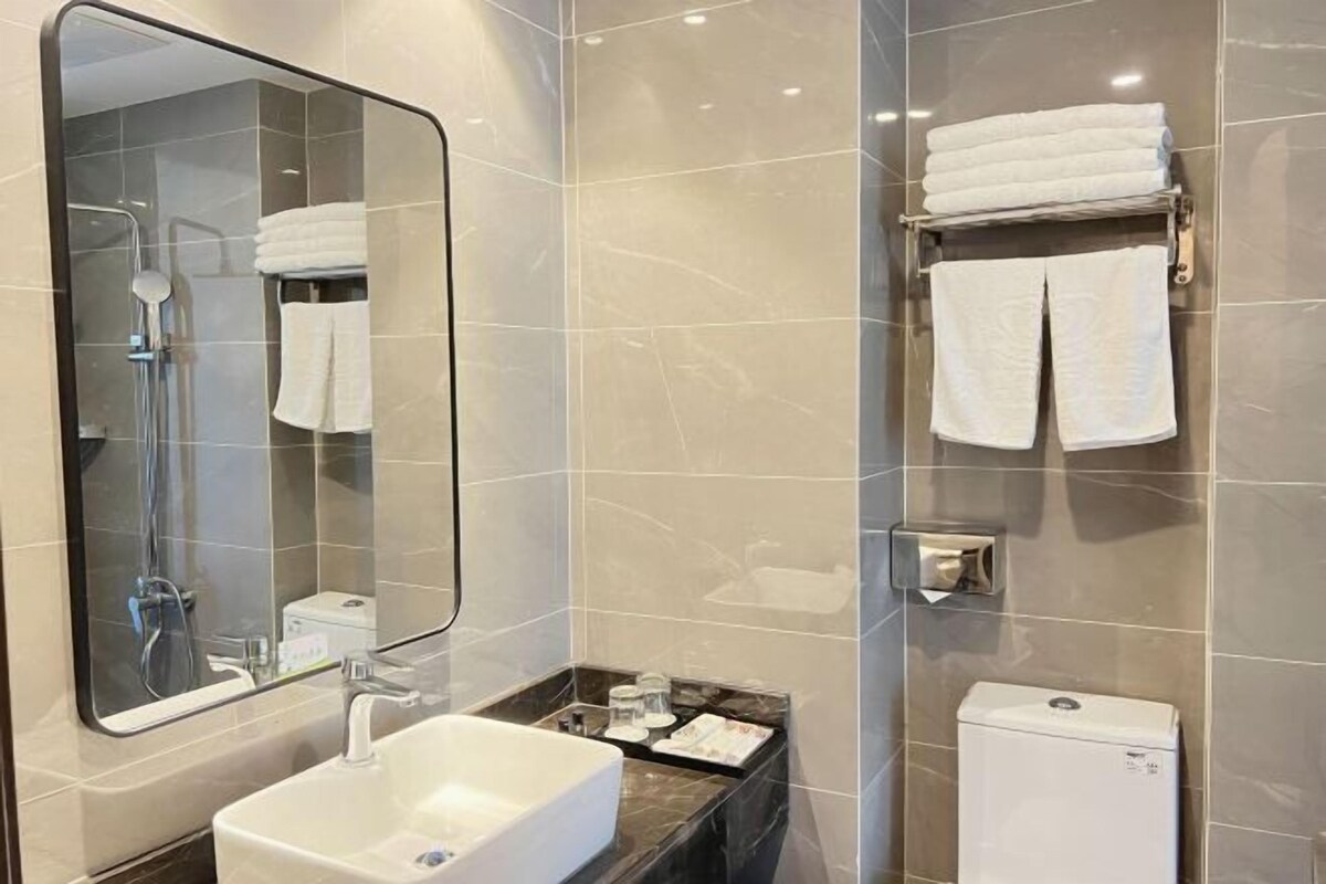 A modern bathroom with a large mirror, a bathtub, a toilet, and a towel rack.