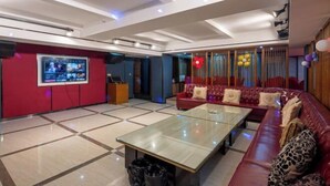 Un hall d’entrée spacieux, avec un canapé rouge, une table basse en verre et un grand écran diffusant du contenu.