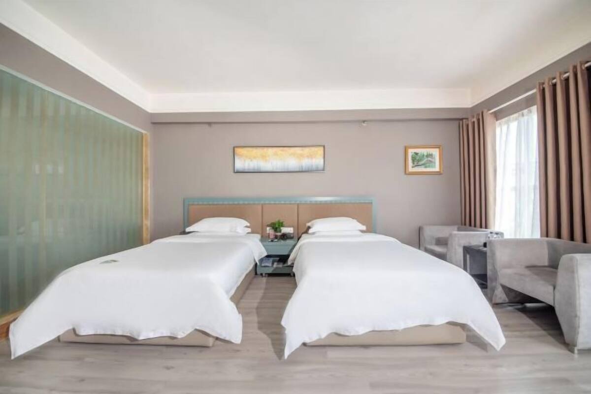 Ein Hotelzimmer mit zwei Betten, einem Nachttisch, einem Sessel und einem Fenster mit Vorhängen.