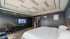 Une chambre d’hôtel moderne dotée d’un grand lit, d’un bureau avec une chaise, d’un téléviseur fixé au mur et d’un tableau encadré accroché au mur.