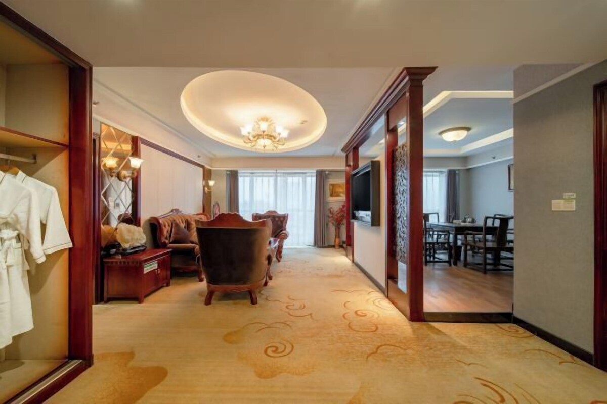 A hotel lobby with a carpeted floor, wooden furniture, a chandelier, and a dining area.