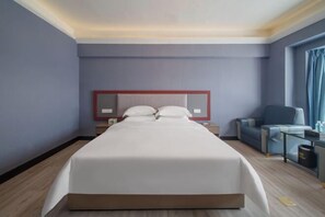 A modern hotel room with a large bed, a bedside table, a chair, and a small table with a lamp. - Ganxian Tianyue International Hotel (Ganxian Qili Ancient Town Resort Branch) (Ganzhou)