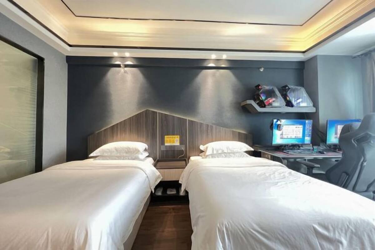 Ein Hotelzimmer mit zwei Betten, einem Schreibtisch mit Computer und einem Regal mit Gegenständen.