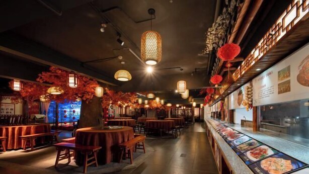 L’intérieur d’un restaurant avec des tables et des chaises en bois, des lanternes suspendues et un comptoir où sont exposés les plats.