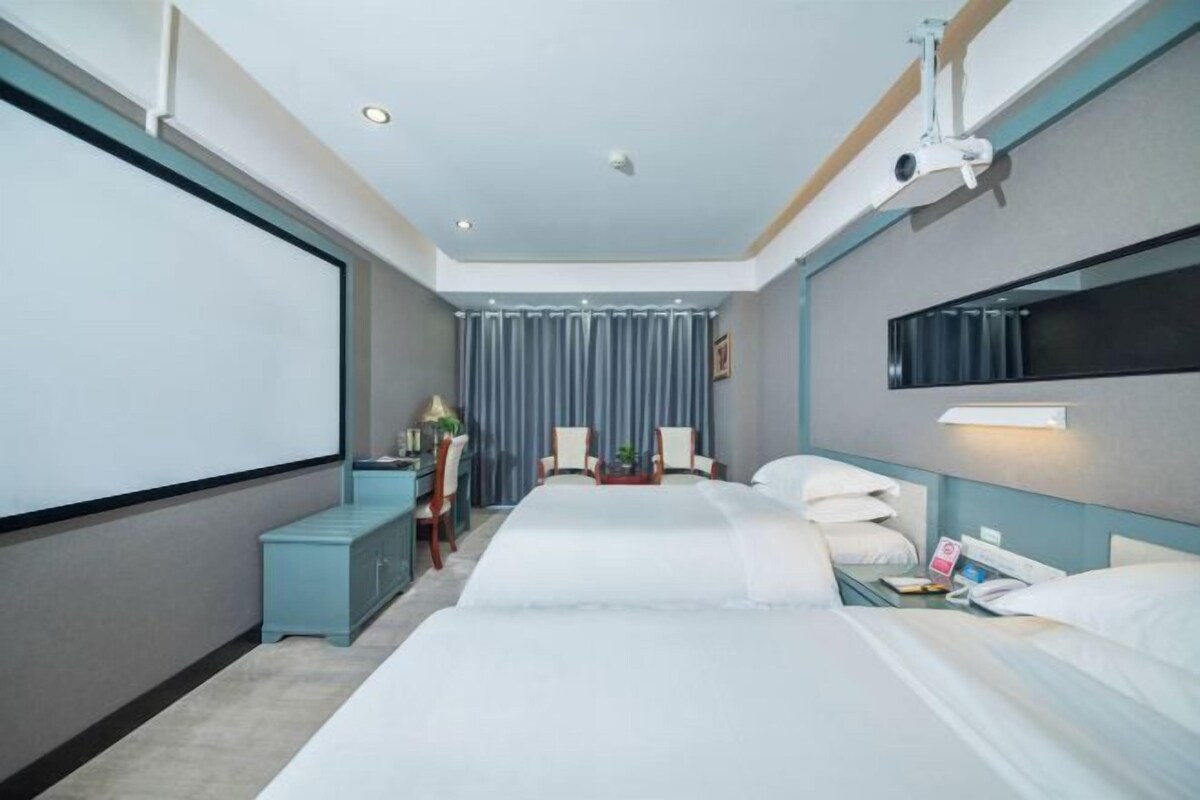 Une chambre d’hôtel avec deux lits, un bureau, une chaise, une télévision et un projecteur.