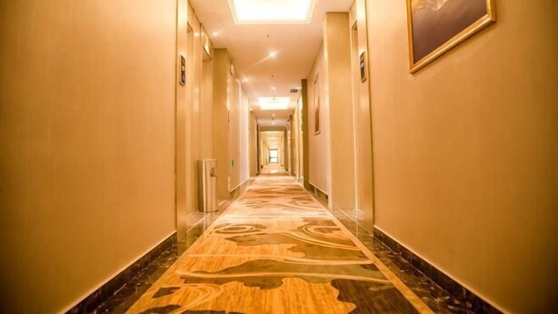 Pasillo de hotel con piso alfombrado, paredes de color claro y una lámpara en el techo.