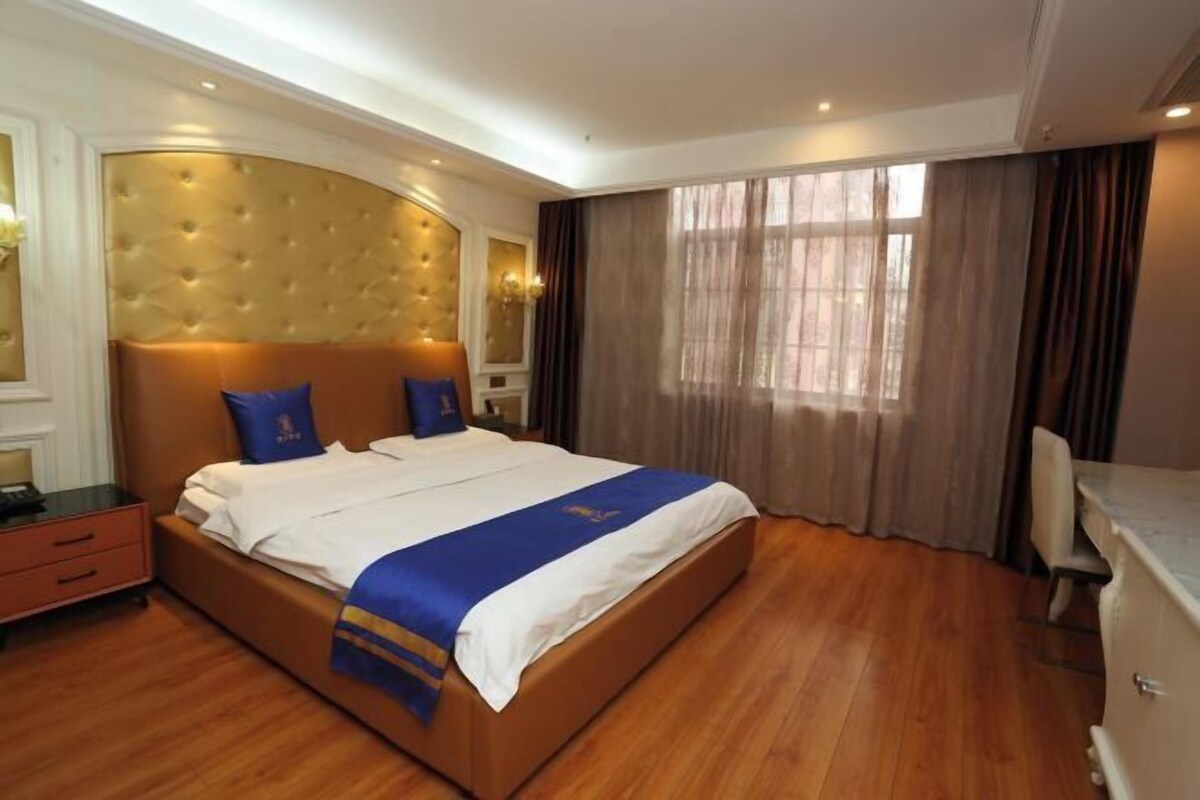 Une chambre d’hôtel avec un grand lit, un plancher en bois, une tête de lit à motifs capitonnés et une fenêtre avec des rideaux.