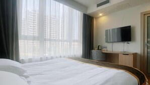 Una habitación de hotel con una cama grande, un televisor montado en la pared y una ventana con cortinas.