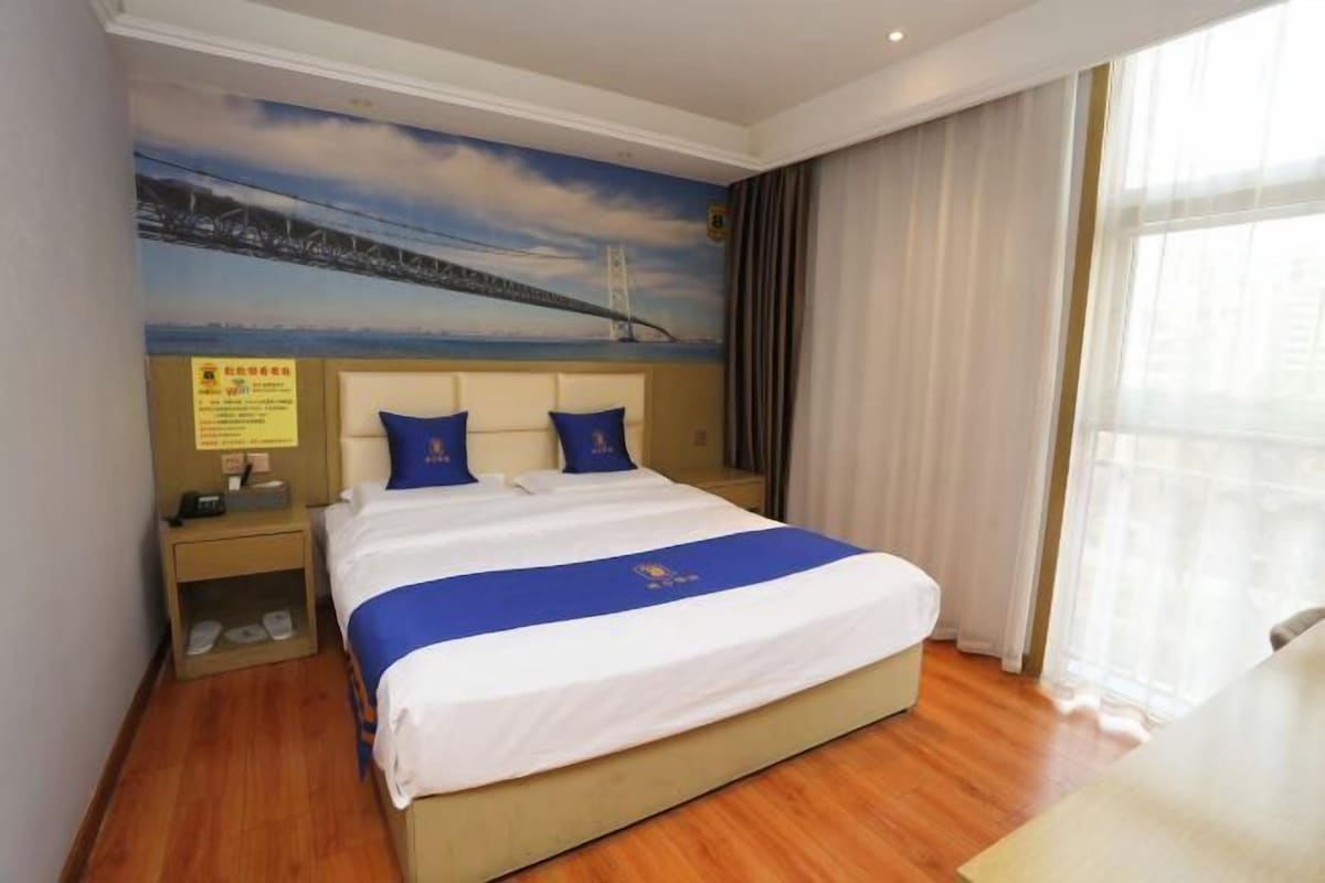 A hotel room with a bed, a nightstand, a wall-mounted TV, and a window with curtains.