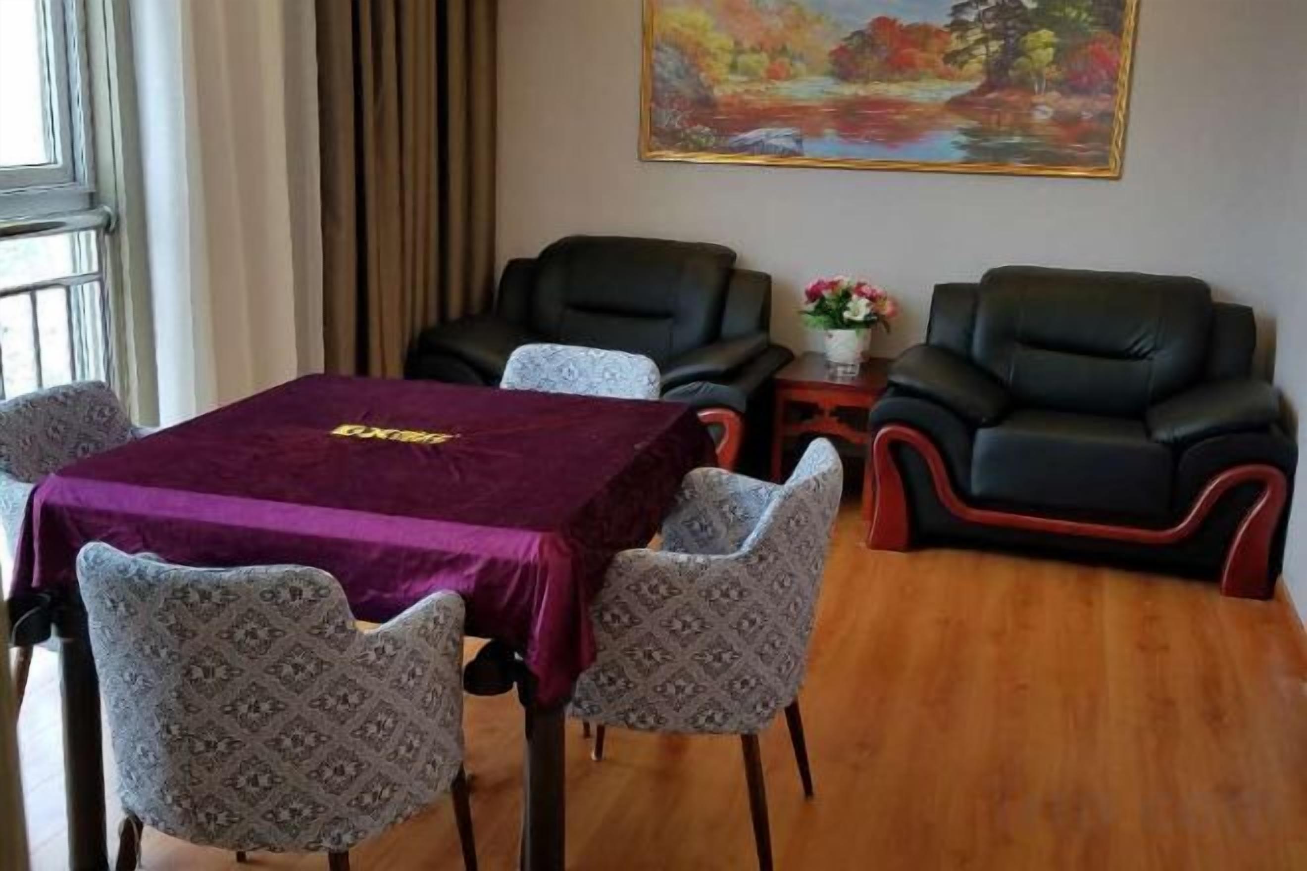 A room with a table, four patterned chairs, two leather sofas, a small side table with a vase, and a painting on the wall.