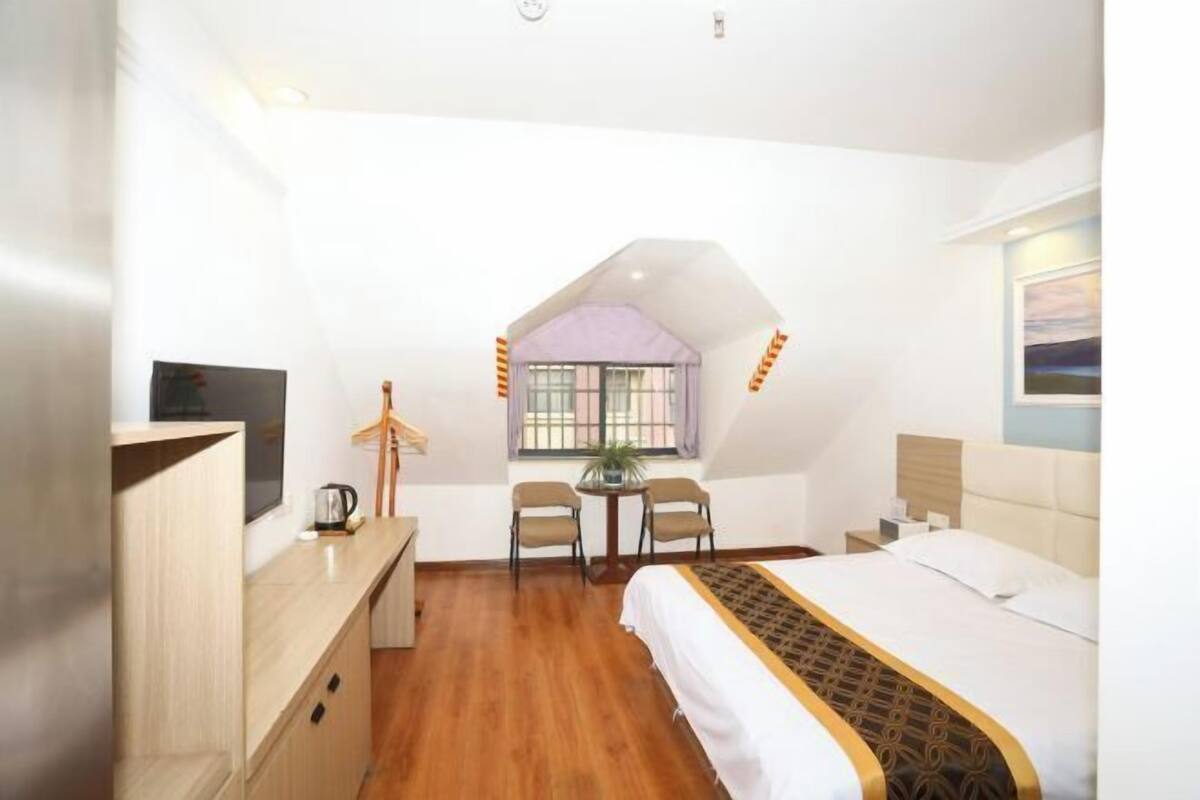 A bedroom with a bed, a desk, a chair, a small table, and a window.