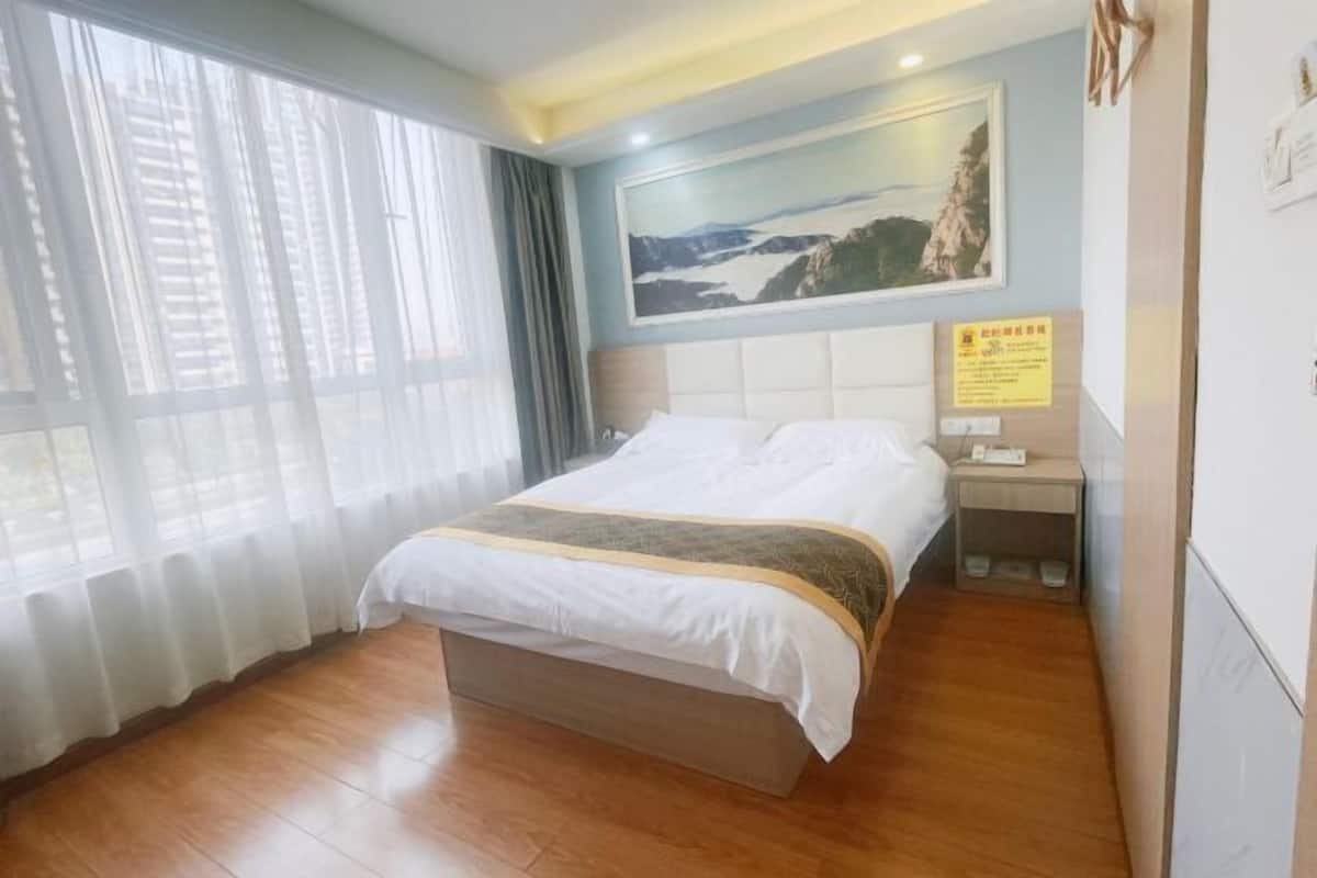 A hotel room with a large bed, a nightstand, a painting on the wall, and a window with curtains.