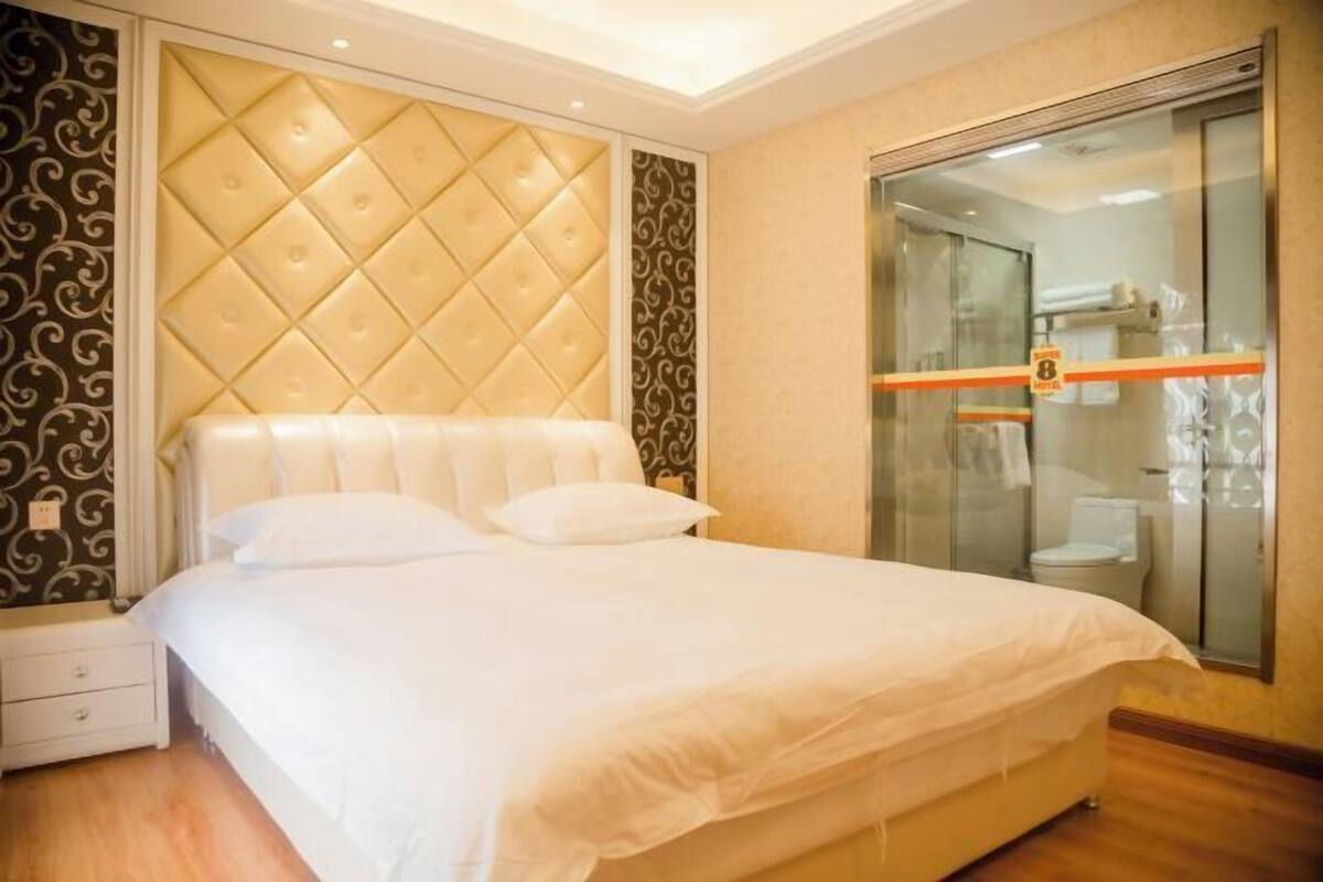 A hotel room with a large bed, a glass shower enclosure, and a visible bathroom.