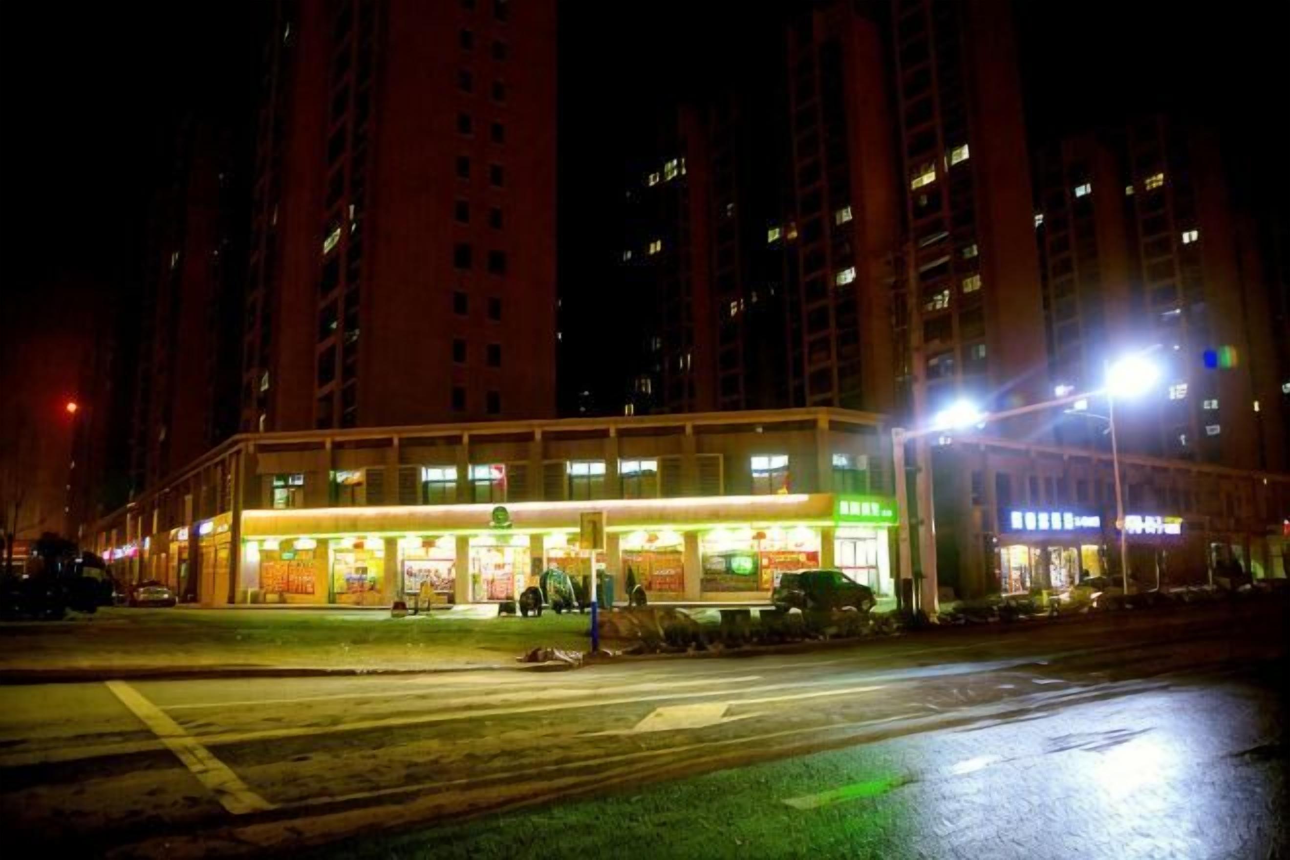 A multi-story building with illuminated signage, a crosswalk, and a wet street at night.