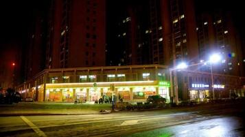A multi-story building with illuminated signage, a crosswalk, and a wet street at night.