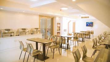 A dining area with multiple tables and chairs, a television screen, and a grill station.