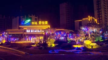 Un hotel muy iluminado con un cartel llamativo, rodeado de árboles y senderos iluminados.
