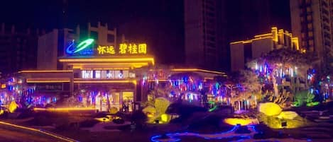 A brightly lit hotel with a prominent sign, surrounded by trees and illuminated pathways.