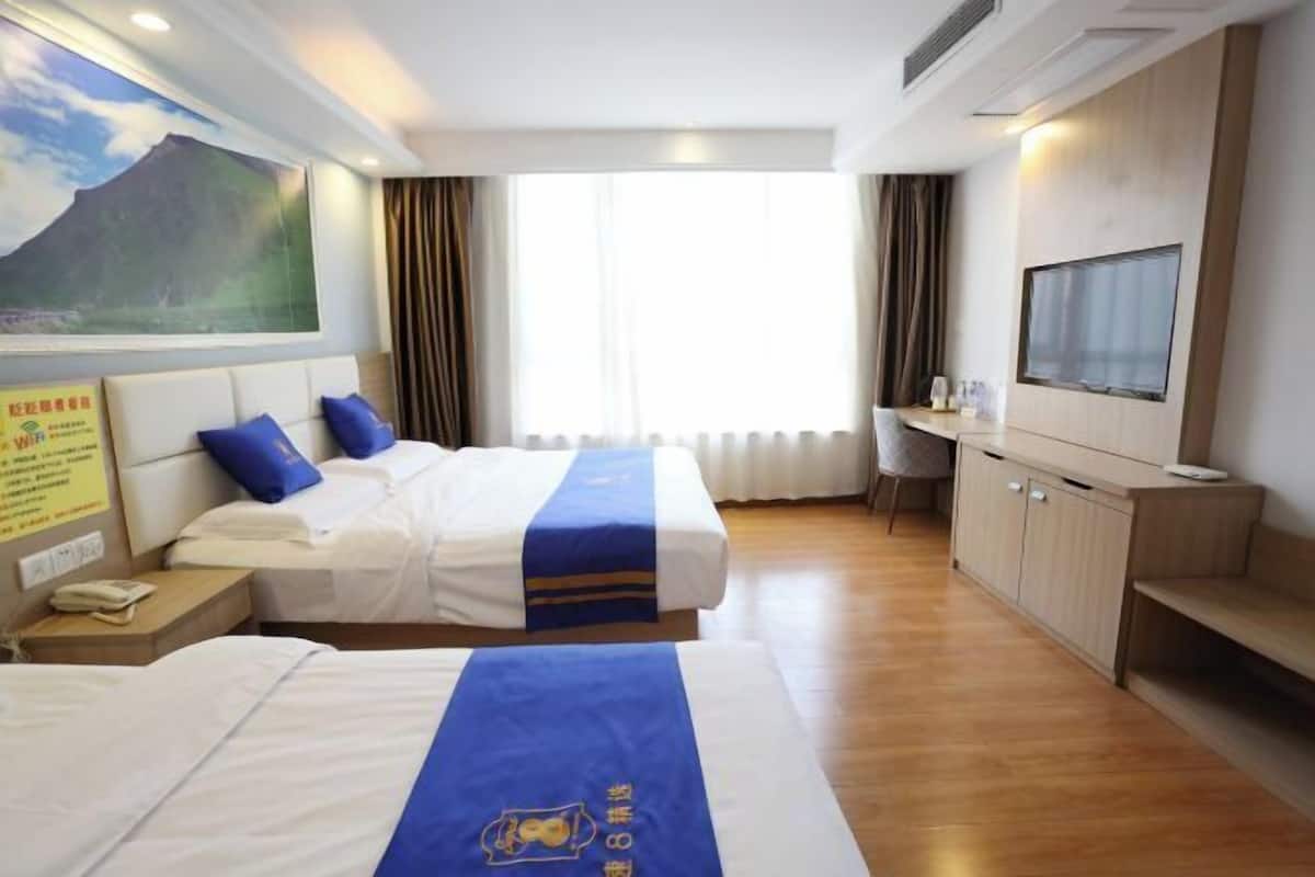 A hotel room with two beds, a desk, a TV, and a large window.