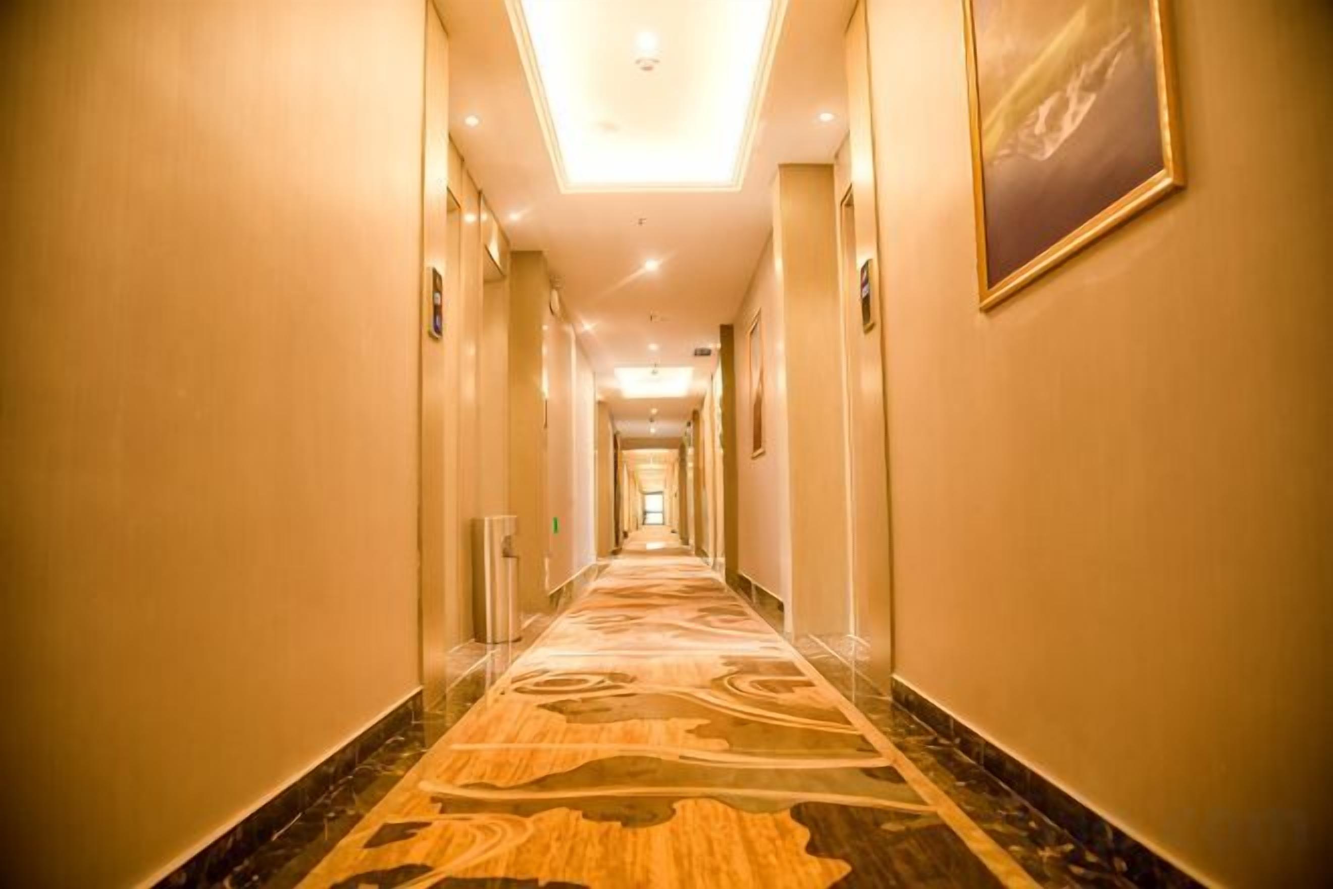 Corredor de hotel com piso coberto por carpete, portas em ambos os lados e uma luminária no teto.