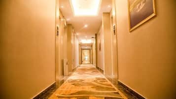 Corredor de hotel com piso coberto por carpete, portas em ambos os lados e uma luminária no teto.